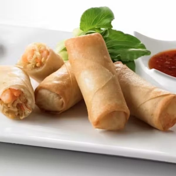 Golden-brown spring rolls with visible shrimp and vegetables, served with chili sauce and bok choy.