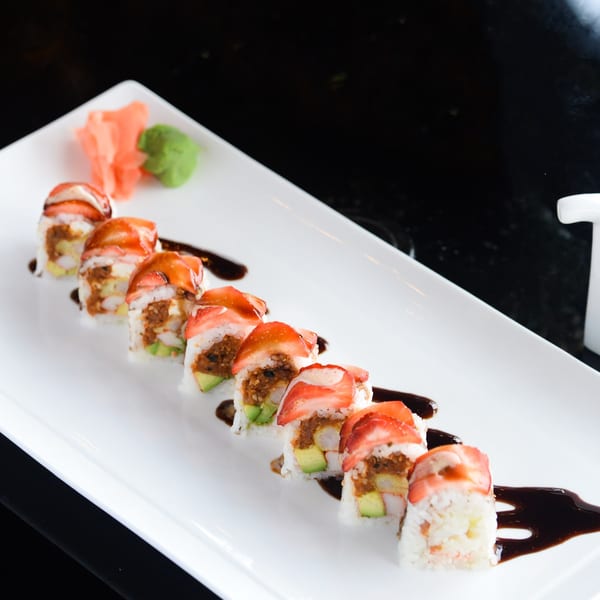 Strawberry-topped sushi rolls with avocado and sauce on a white rectangular plate.