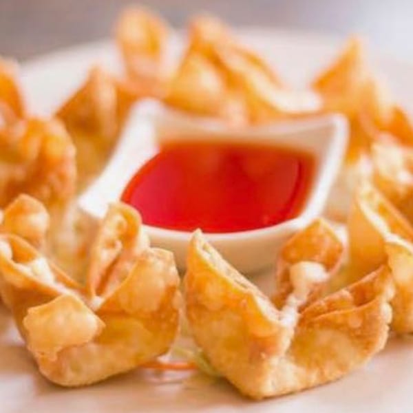 Crispy golden-brown crab rangoon appetizers arranged around a small dish of red dipping sauce.