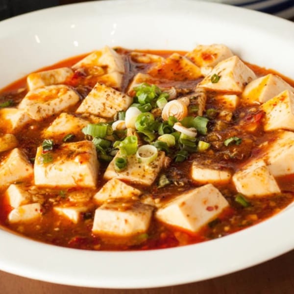 A white bowl filled with Mapo Tofu, featuring cubes of tofu in a spicy red sauce, garnished with green onions.