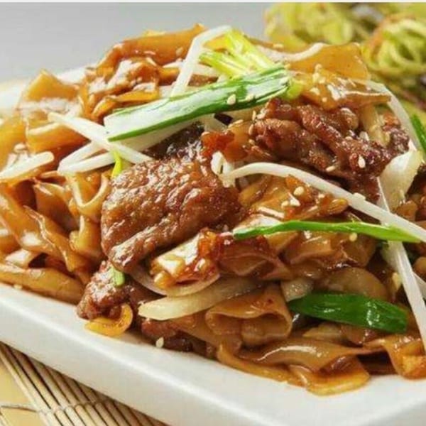 Beef chow fun with wide noodles, bean sprouts, onions, and green onions on a white plate.